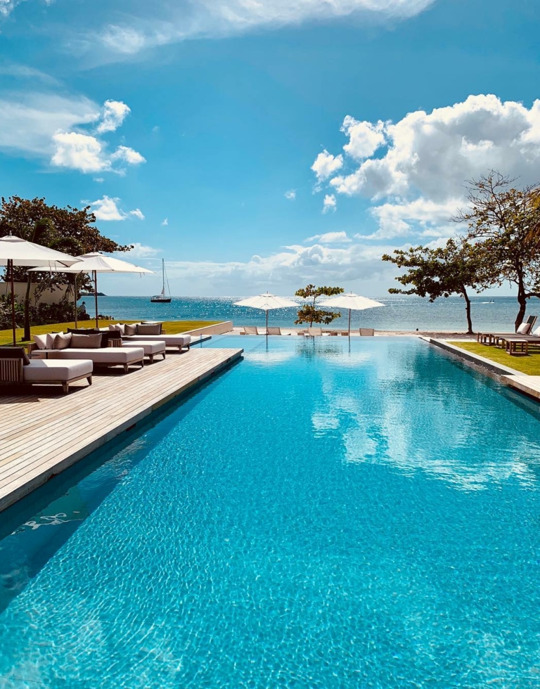 Terrasse softline en teak et ipé entourant grande piscine donnant sur mer avec ciel bleu dégagé